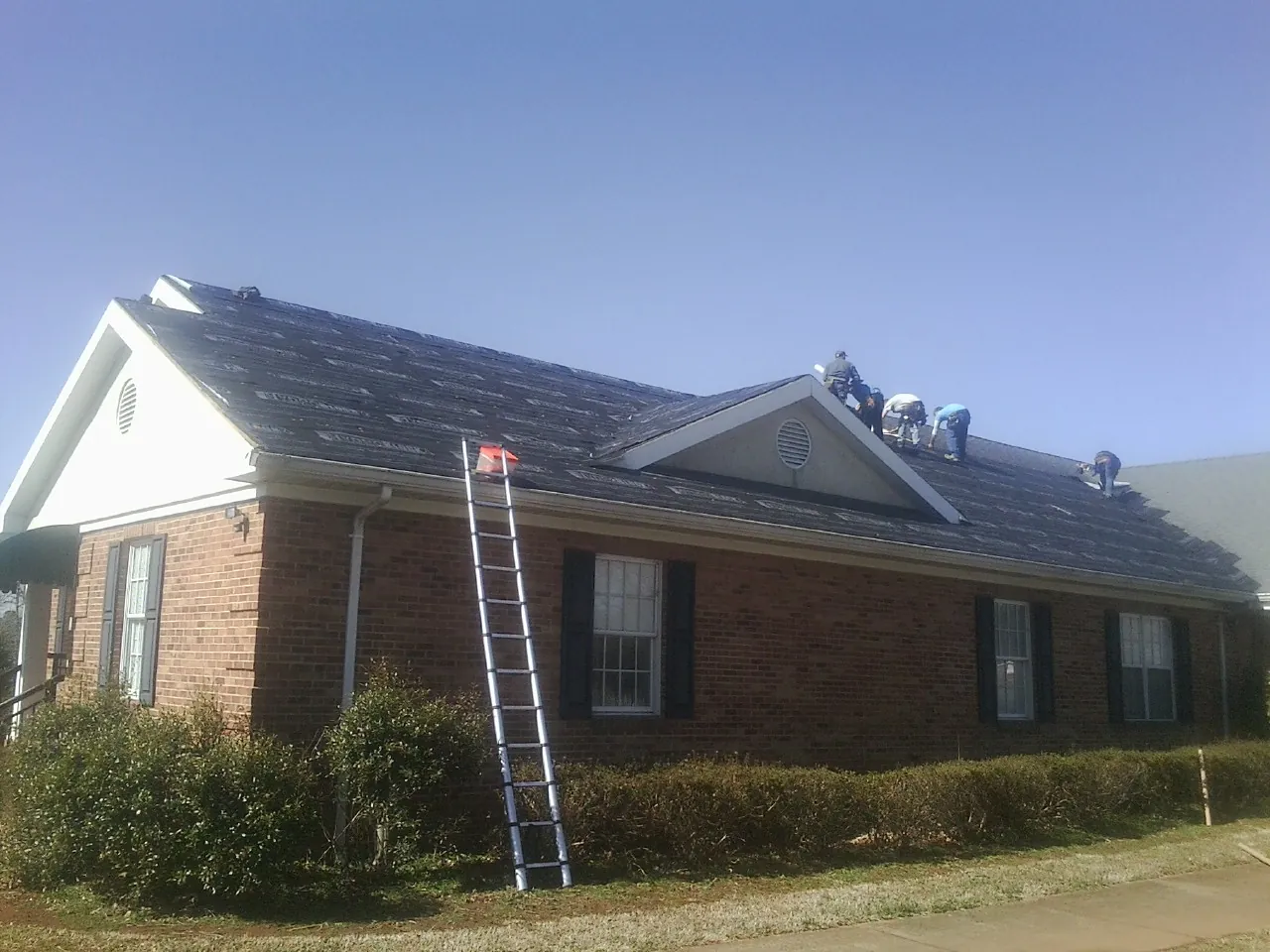 Crew tearing shingles off a brick ranch roof with a ladder set — Emergency Roof Repair work by our crew in Vauxhall